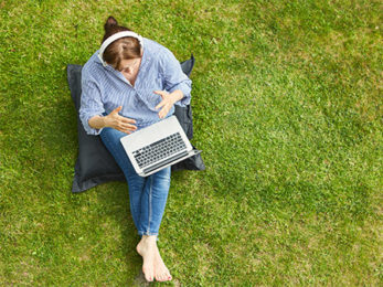 Junge Frau bei einem Online-Meeting, auf einer Wiese sitzend