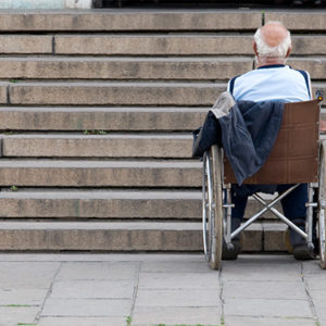 Mann im Rollstuhl steht vor einer Treppe, die eine große Barriere darstellt