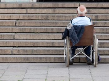 Mann im Rollstuhl steht vor einer Treppe, die eine große Barriere darstellt