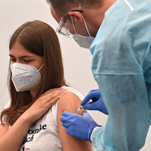 Das Foto zeigt eine Schülerin, Jugendliche die geimpft wird. Arzt und Schülerin tragen Masken zum Schutz vor Ansteckung.