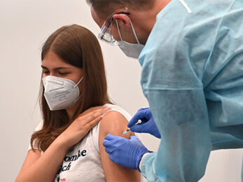 Das Foto zeigt eine Schülerin, Jugendliche die geimpft wird. Arzt und Schülerin tragen Masken zum Schutz vor Ansteckung.