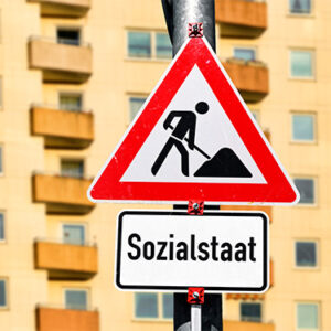 Baustellenschild mit Aufschrift Sozialstaat vor Wohngebäude, Symbolfoto für den Umbau des Sozialsystems, Fotomontage