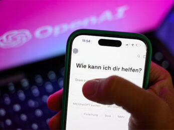 Dieses Foto zeigt ein Smartphone. Auf dem Bildschirm ist die Benutzeroberfläche einer KI zu sehen mit dem Schriftzug: Wie kann ich dir helfen?